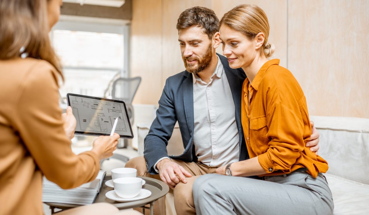 Young and lovely couple choosing a new house to buy, looking on the projects with a sales manager in the office of real estate agency